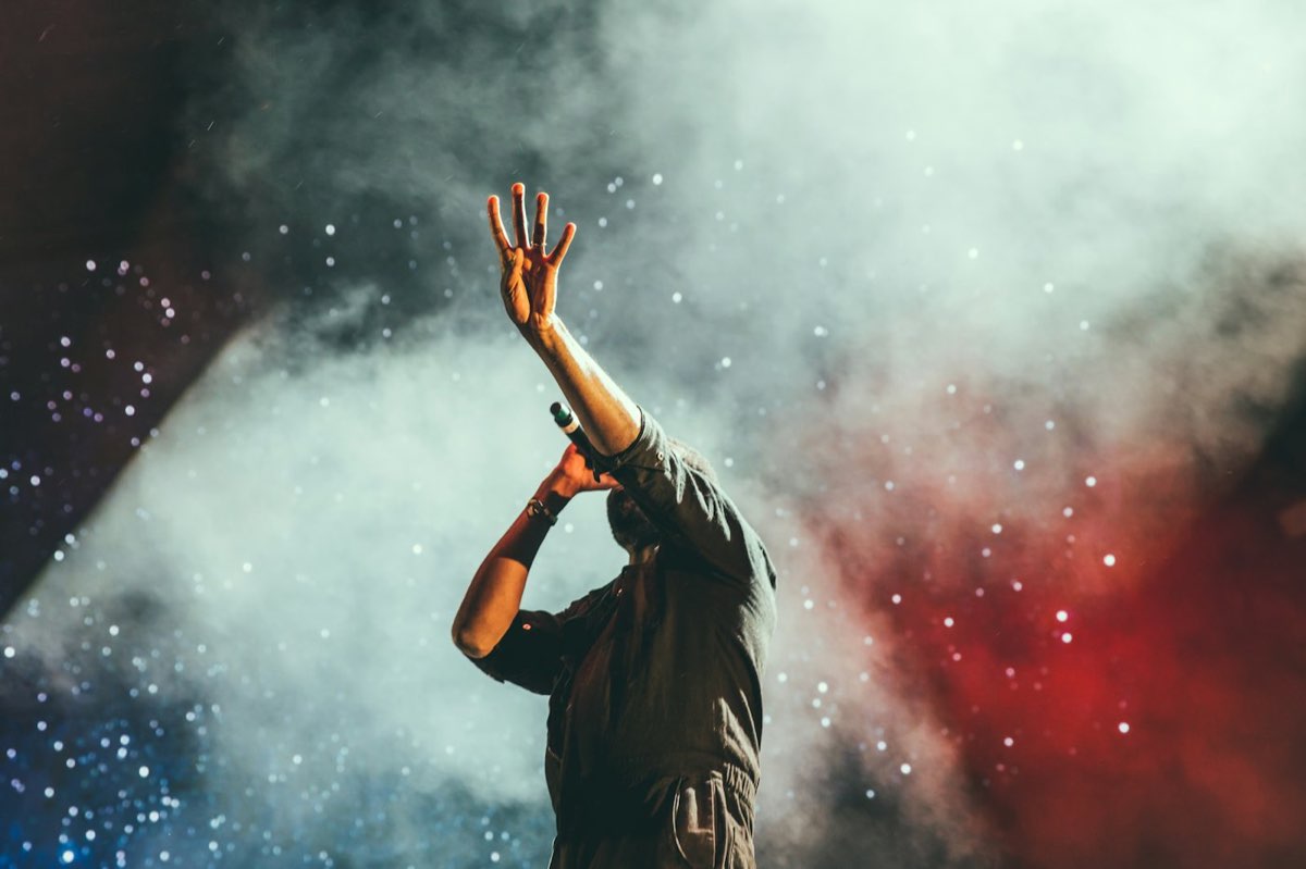 Artista en un escenario con la mano en alto entre humo y luces